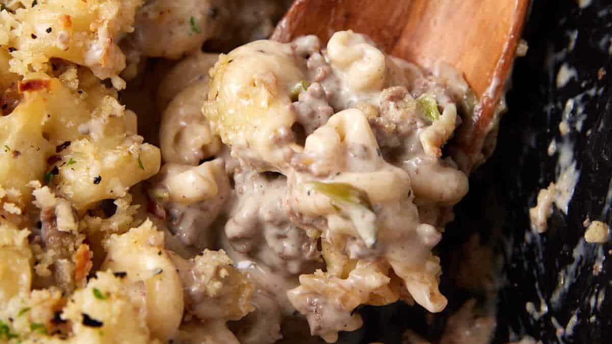 Close-up of a creamy macaroni and ground beef casserole—one of our favorite unique casserole recipes—being scooped with a wooden spoon.