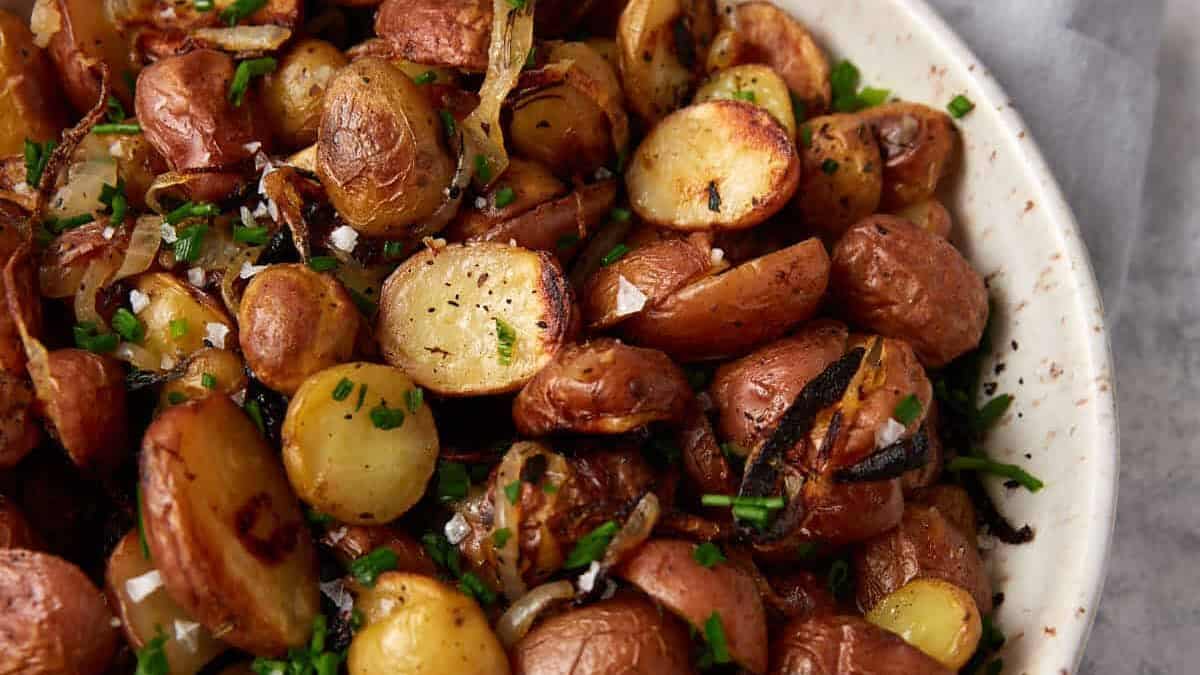 A bowl of roasted baby potatoes with crispy edges, garnished with chopped herbs and caramelized onions—perfect for fall dinners and a delicious addition to your collection of potato side dishes.