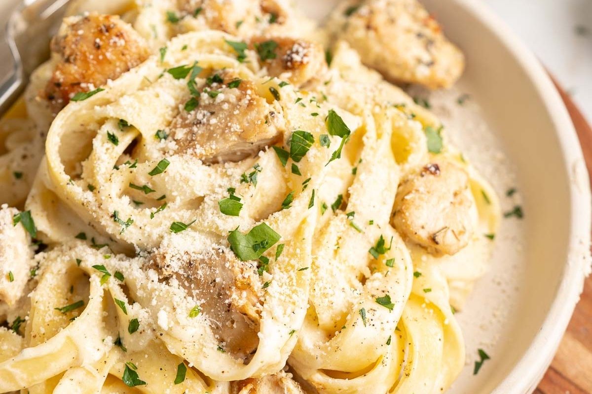 Fettuccine pasta with creamy Alfredo sauce, grilled chicken pieces, grated Parmesan cheese, and chopped parsley served in a bowl—a classic recipe that brings timeless flavors to your table.