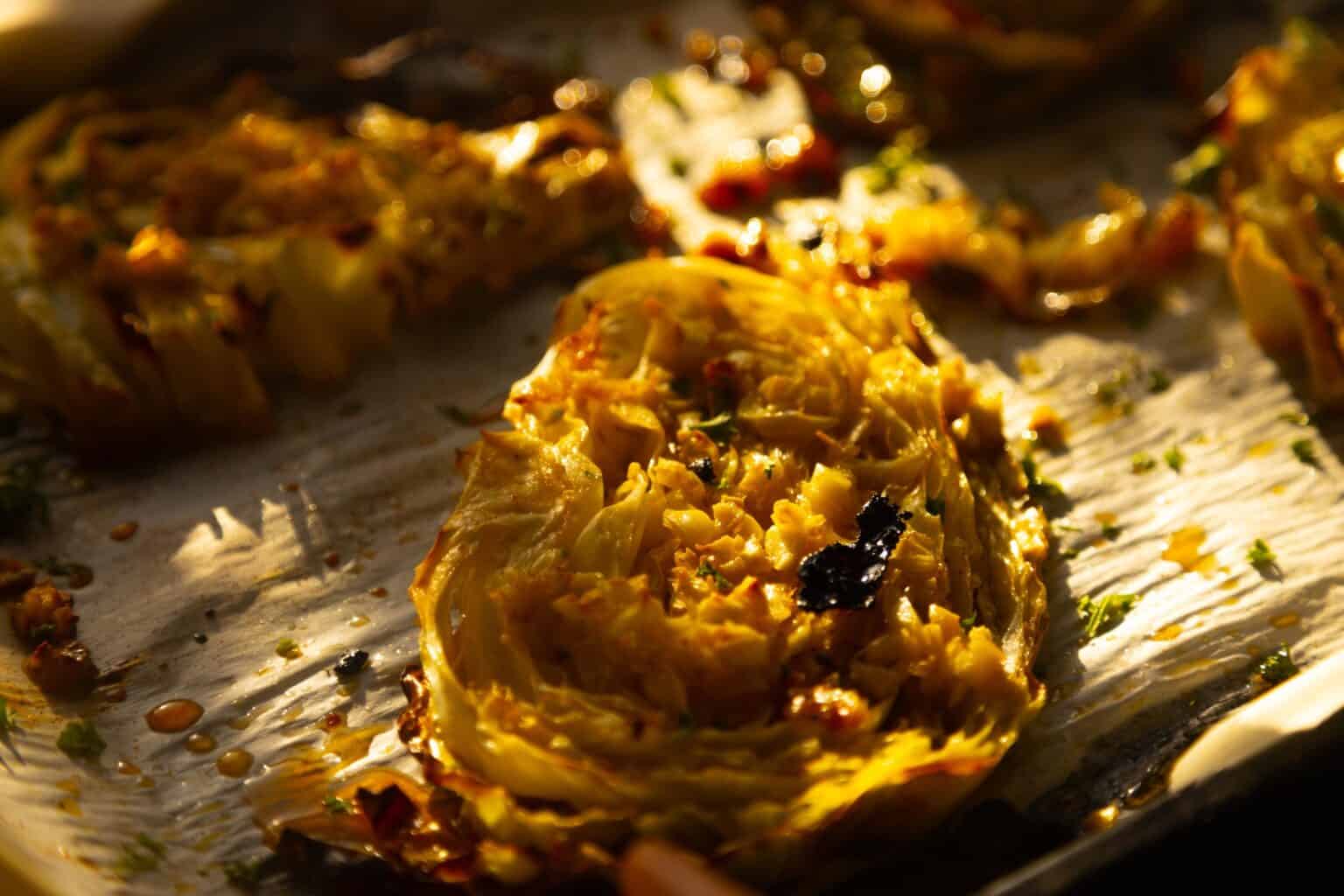 Close-up of roasted cabbage wedges on a baking sheet, with visible charring and seasonings under warm lighting—an inviting addition to your collection of healthy recipes or anyone seeking creative cabbage recipes.