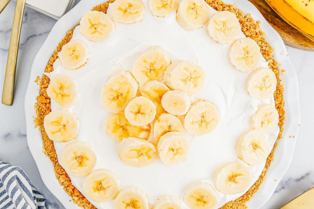A banana cream pie topped with whipped cream and sliced bananas, displayed on a white plate—one of those classic recipes that never goes out of style.