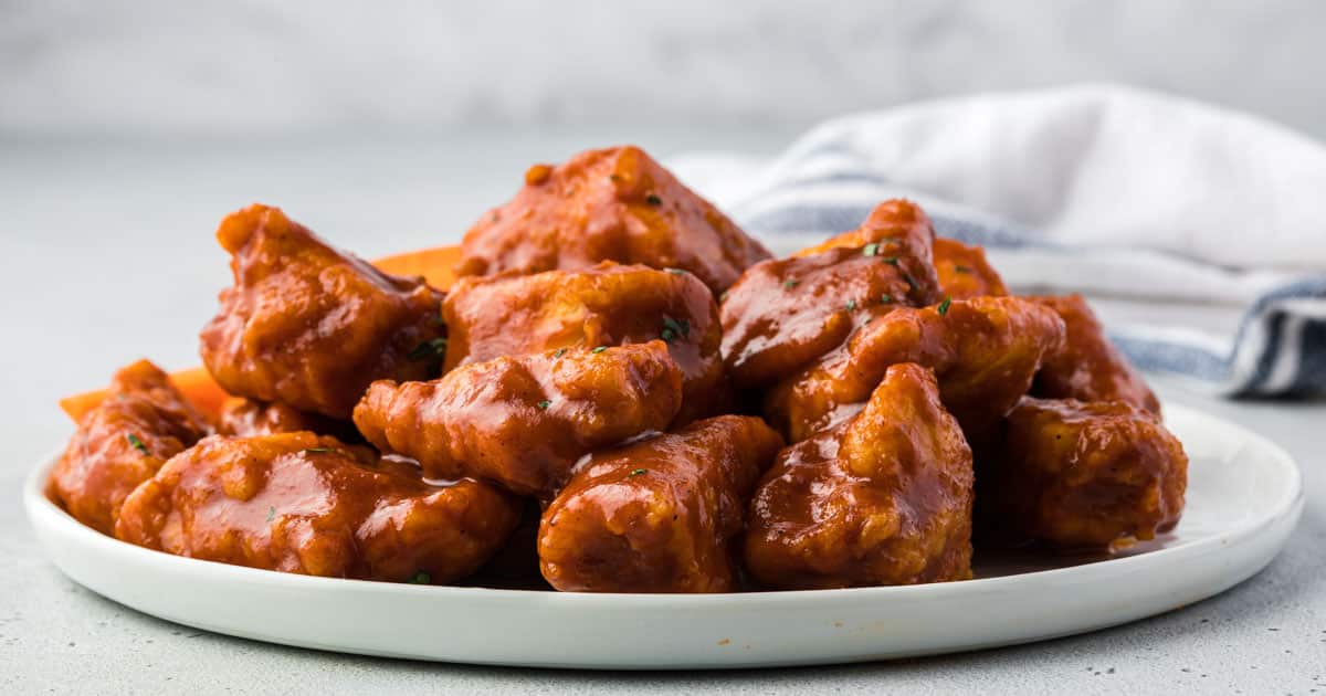 Plate of saucy boneless buffalo chicken wings arranged on a white dish—perfect Game Day Food for your collection of Chicken Wing Recipes. Striped towel in the background.