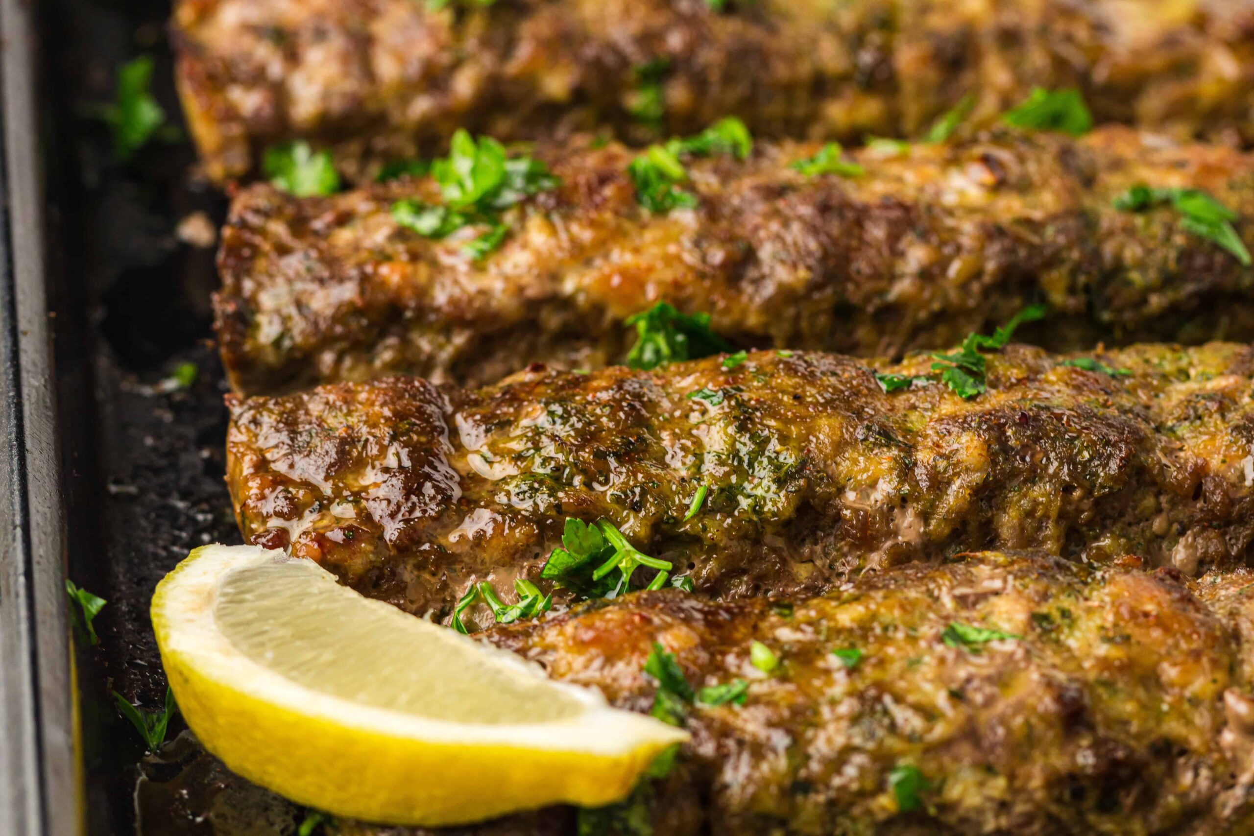 Four grilled kebabs garnished with chopped parsley are arranged on a tray with a lemon wedge placed at the corner, making this dish a perfect choice for easy sheet pan meals or quick weeknight dinners.