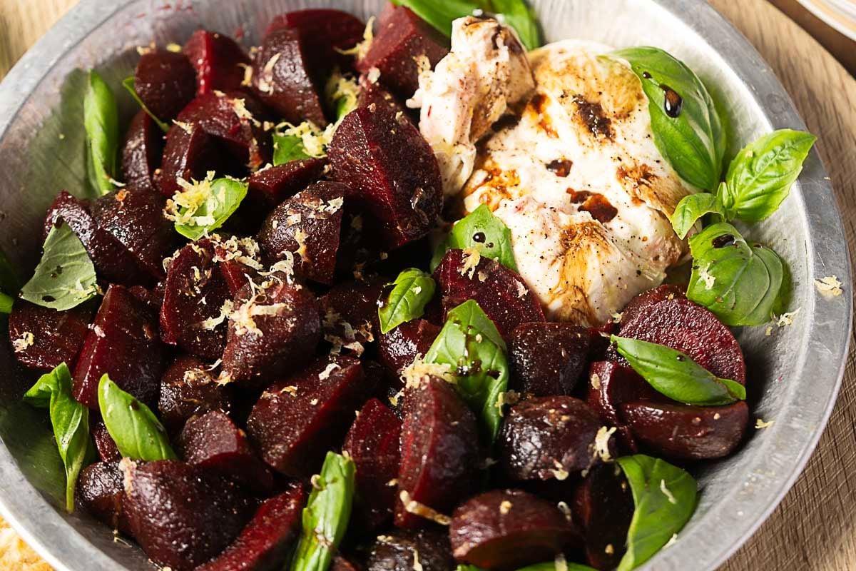 A metal bowl contains roasted beet chunks, fresh basil leaves, a dollop of soft cheese, and a sprinkle of lemon zest—an inviting combination perfect for autumn salads.