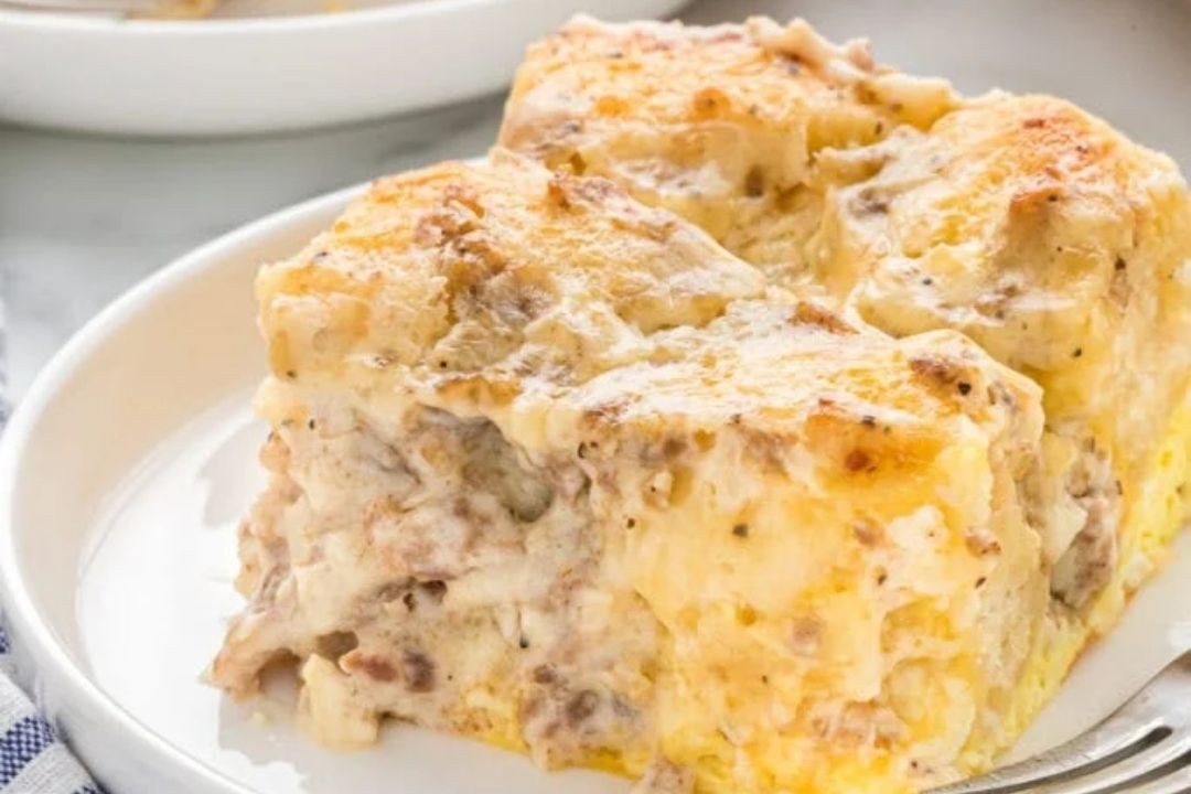 Two square pieces of creamy sausage breakfast casserole with a golden cheese topping are served on a white plate—a delicious example of savory breakfasts that’s perfect for your morning table.