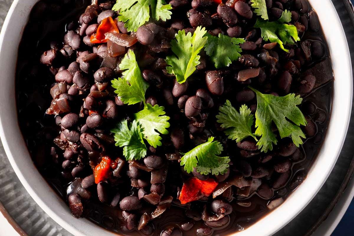 A bowl of black beans garnished with fresh cilantro leaves and small pieces of red pepper, perfect for anyone looking to add bold flavor to their Tex Mex dinner recipes.