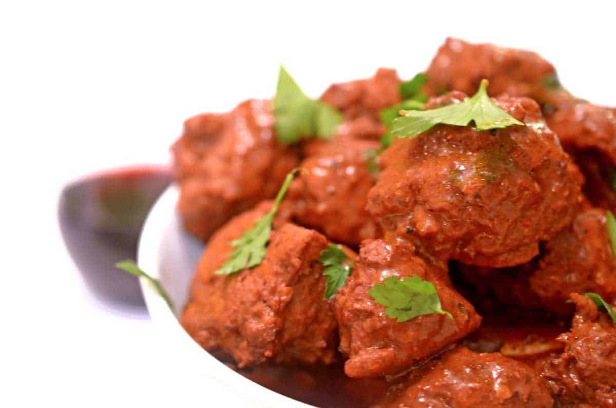 A close-up of red, marinated meat pieces garnished with fresh cilantro, perfect for cozy braises, served in a white bowl on a white background.