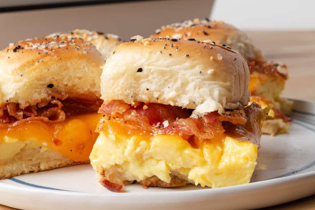 Breakfast sliders with scrambled eggs, cheddar cheese, and bacon on everything-seasoned rolls, served on a white plate—a perfect addition to your collection of savory breakfast recipes.