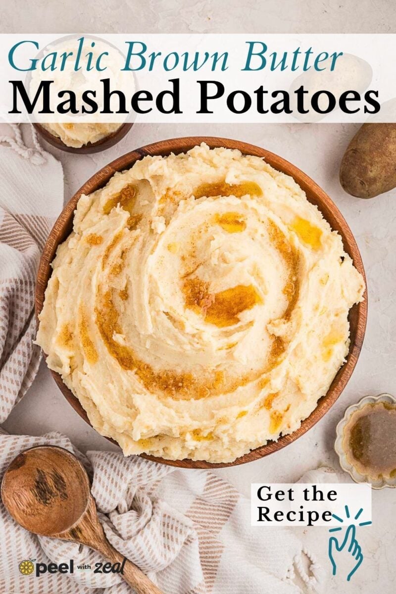 Bowl of brown butter mashed potatoes with a rich brown butter swirl, surrounded by potatoes, a wooden spoon, and a small dish on a textured cloth. Text overlay promotes a garlic brown butter recipe.