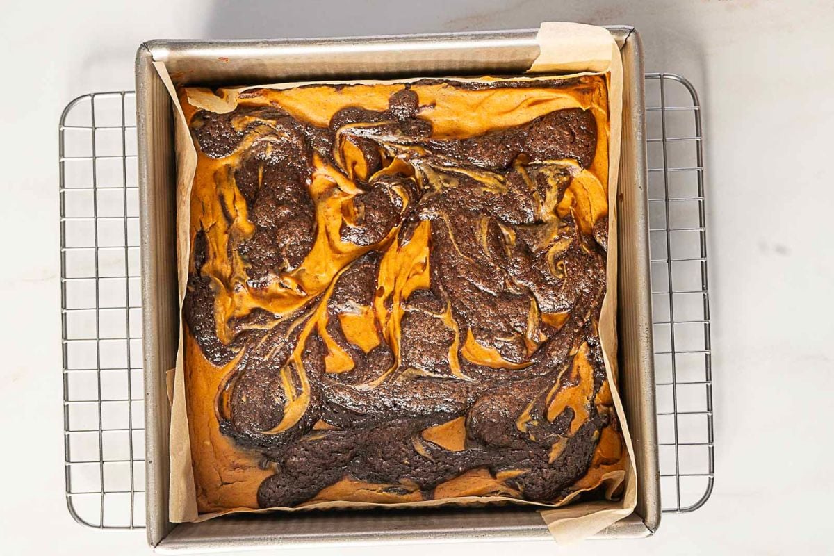 A square pan of gluten free swirled cheesecake brownies cools on a rack, featuring a marbled pattern of chocolate and cheesecake—a standout among gluten free desserts.