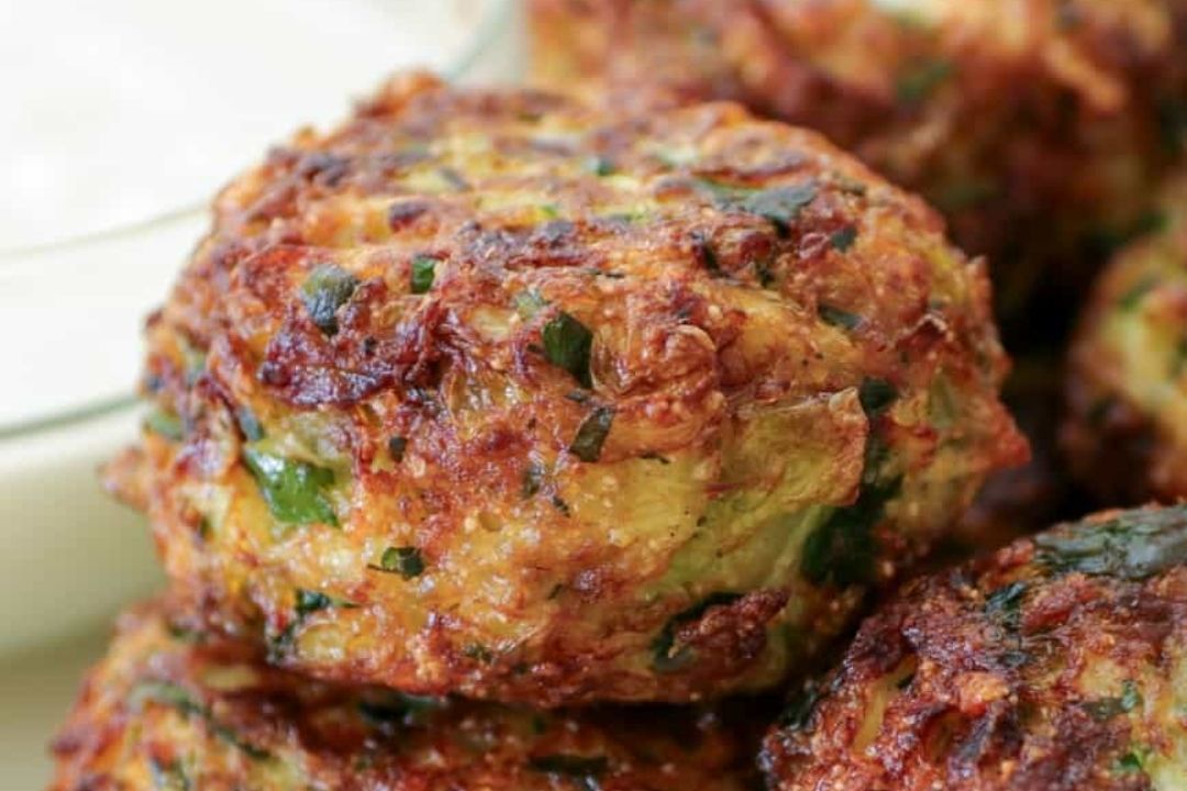 Close-up of crispy, golden-brown fritters with visible green herbs, stacked together on a plate—an irresistible twist on classic cabbage dishes.