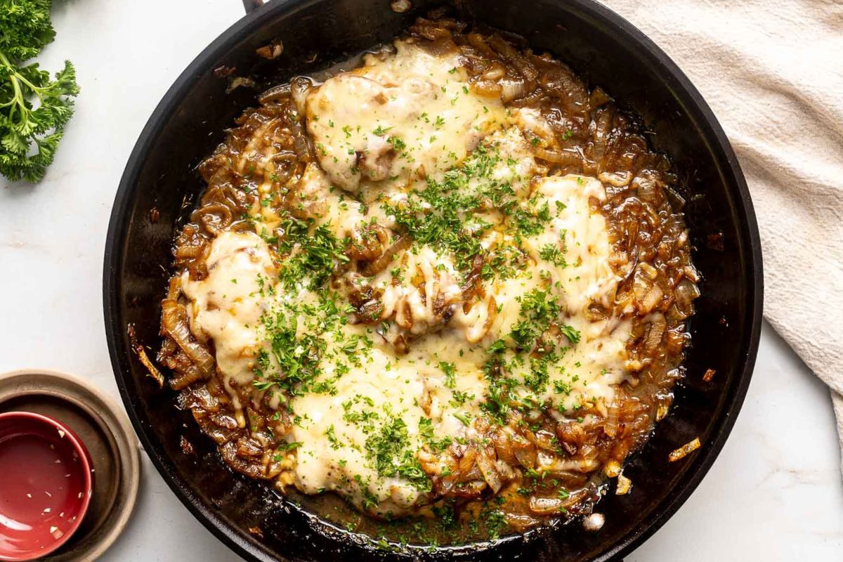 A skillet filled with cooked chicken breasts topped with melted cheese, caramelized onions, and chopped parsley makes one of the best quick meals for busy nights. This delicious dish is perfect for anyone looking for easy casseroles or dinner recipes that come together effortlessly.