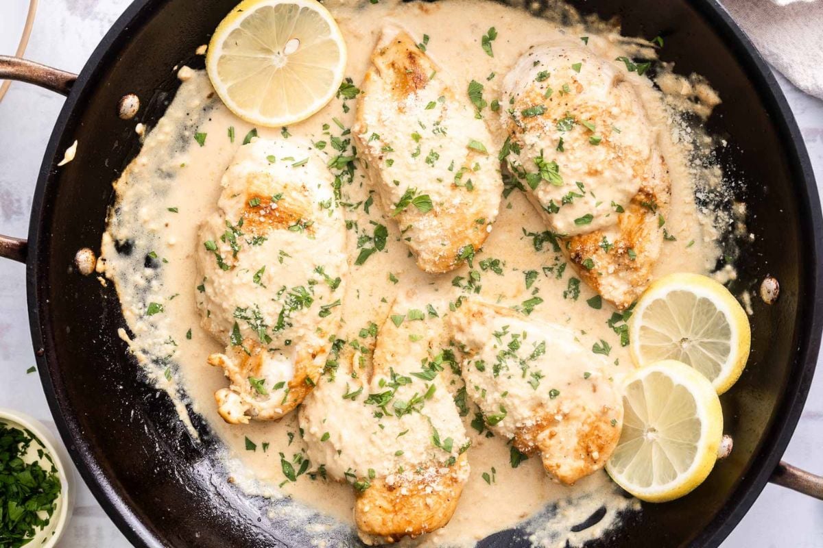 Chicken breasts in a creamy sauce are garnished with chopped herbs and lemon slices in a black skillet, making this one of those perfect Family Dinner Recipes that's both delicious and Kids Friendly.