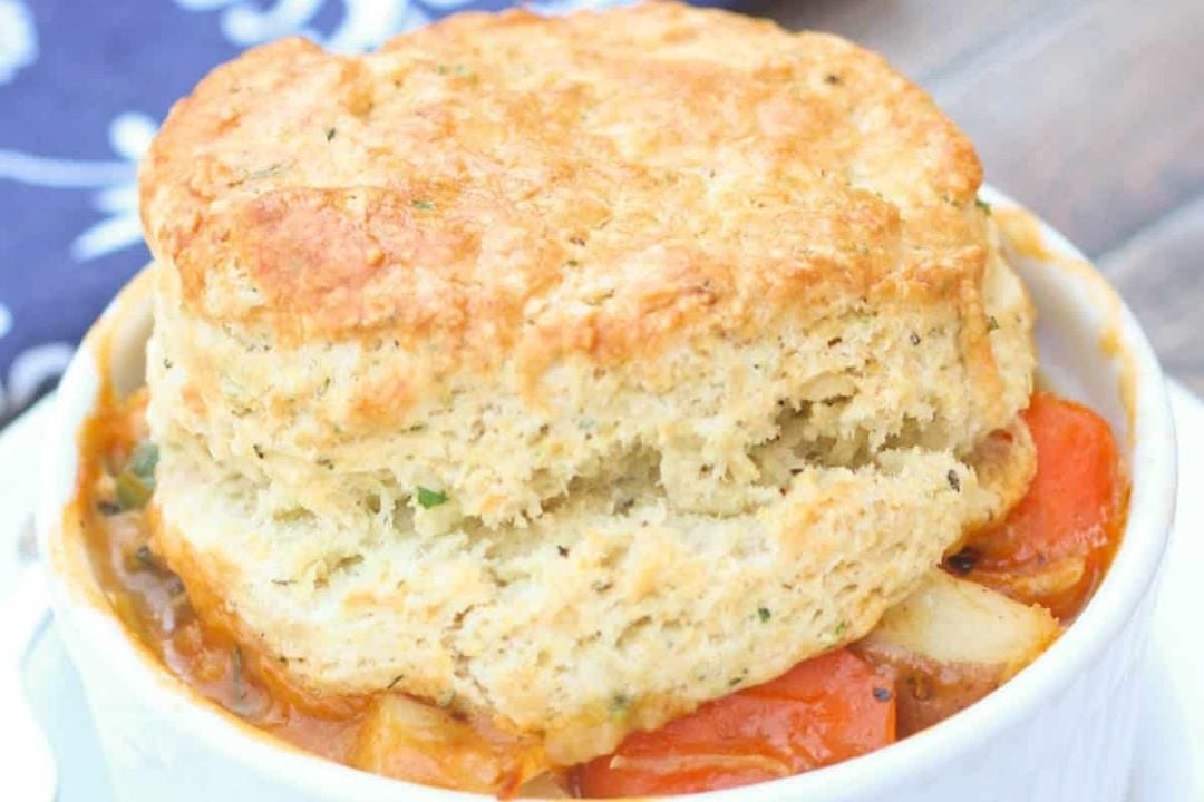 Biscuit-topped vegetable stew in a white bowl, showing carrots, potatoes, and thick, golden biscuit crust—a comforting dish inspired by timeless recipes.