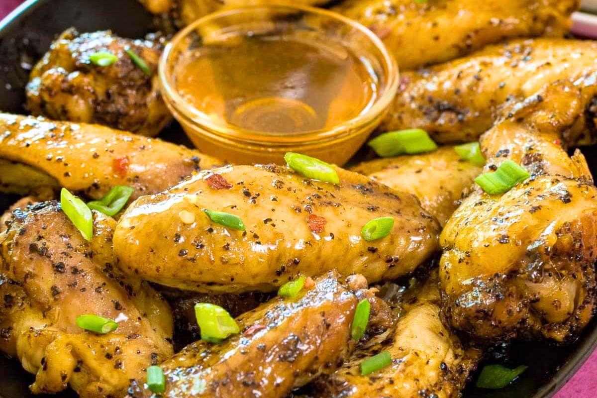 Chicken wings coated with black pepper and herbs, garnished with green onions—an ideal choice for chicken wing recipes or tasty game day appetizers, served with a tangy dipping sauce.