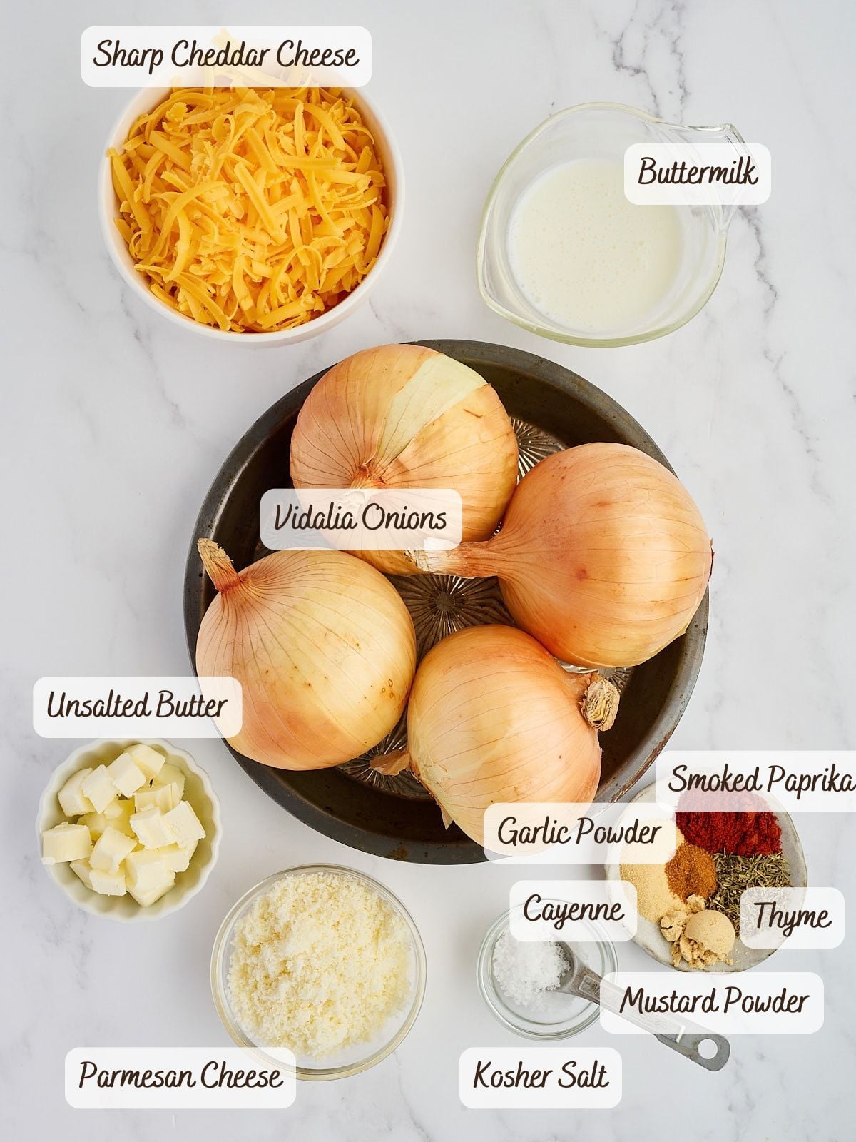 A plate with Tennessee onions is surrounded by bowls of sharp cheddar, Parmesan, butter, buttermilk, garlic powder, cayenne, thyme, smoked paprika, mustard powder, and kosher salt.