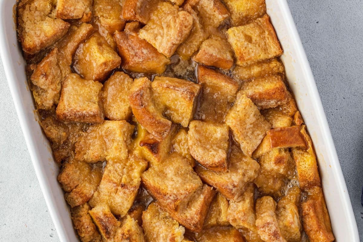A close-up of baked bread pudding in a white dish, showcasing golden-brown bread pieces soaked in a caramel-colored custard mixture—a unique casserole that stands out among classic casserole recipes.