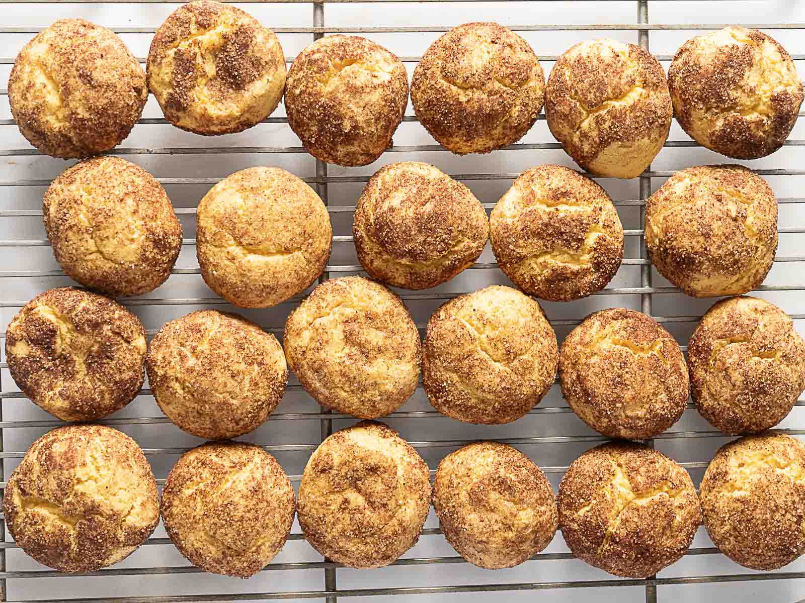 Twenty-four golden brown gluten free muffins cooling on a metal wire rack, evenly spaced in rows with visible sugar topping.