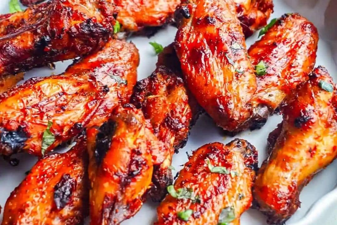 A plate of grilled chicken wings with a charred exterior, garnished with green herbs—perfect for game day appetizers or halftime snacks.