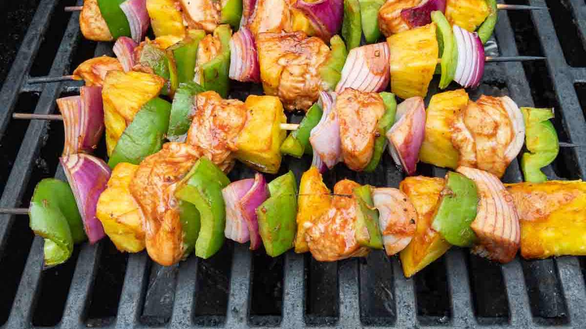 Skewers with grilled chicken, green bell peppers, red onions, and pineapple chunks are cooking on a grill—perfect for easy chicken recipes and quick weeknight meals.