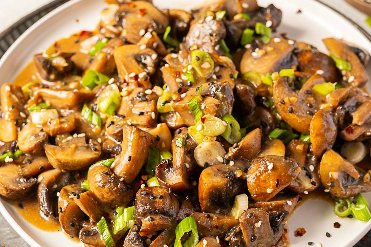 Sautéed mushrooms garnished with chopped green onions and sesame seeds, served on a white plate—one of the best side dishes that’s sure to be a show-stealing recipe at any meal.