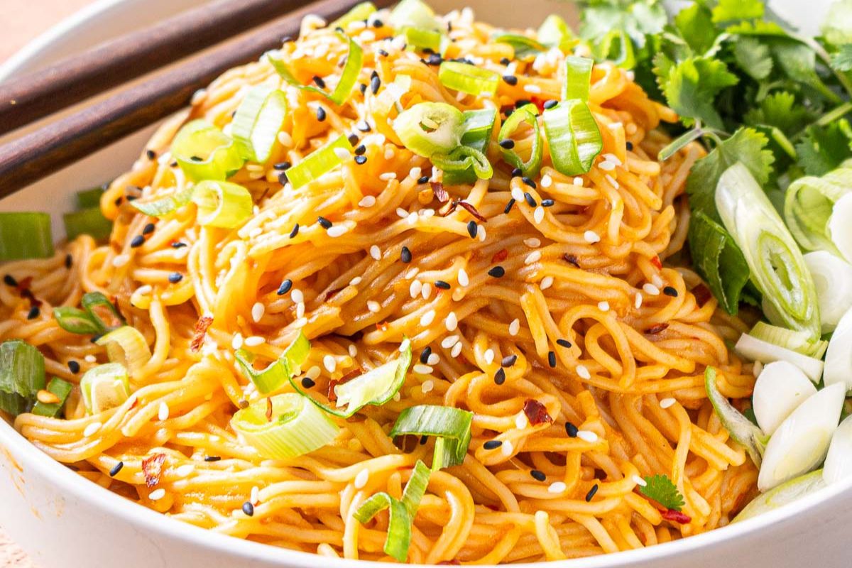 A bowl of noodles topped with sesame seeds, chopped green onions, and cilantro, with chopsticks resting on the side—perfect for those seeking delicious dinner ideas or looking to try popular recipes at home.