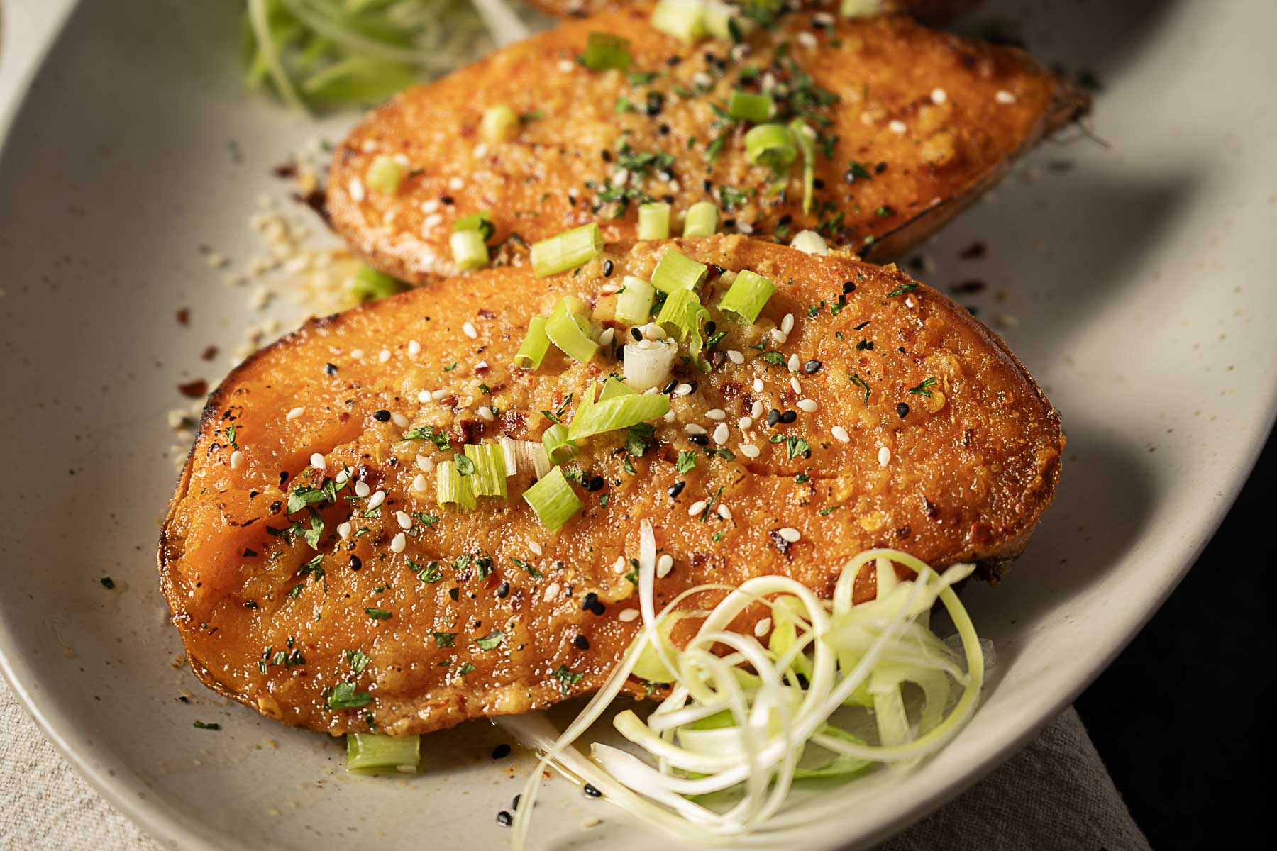 Two roasted sweet potato halves topped with green onions, sesame seeds, and spices—a delicious addition to your favorite sweet potato recipes.