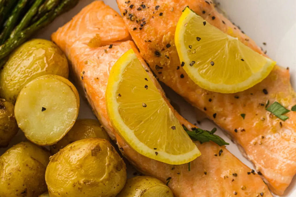 Two baked salmon fillets topped with lemon slices, served with roasted baby potatoes and asparagus on a white plate—an ideal option for easy weeknight dinners or anyone looking for satisfying sheet pan meals.