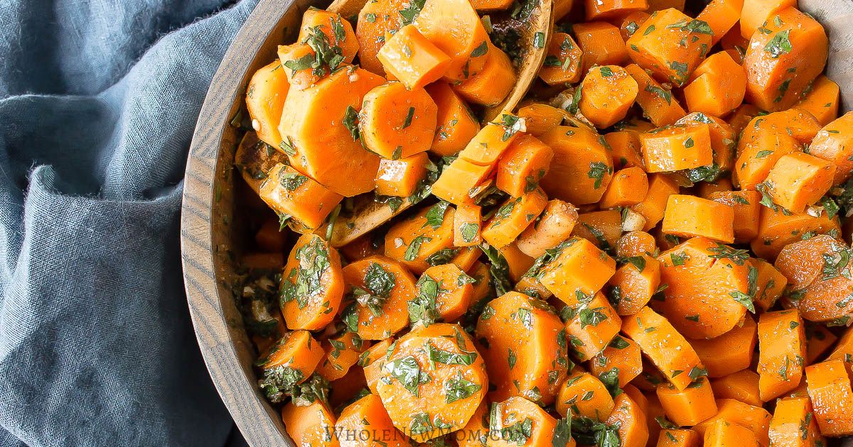 A wooden bowl filled with sliced cooked carrots garnished with chopped herbs, perfect for quick carrot sides, placed on a dark blue cloth.