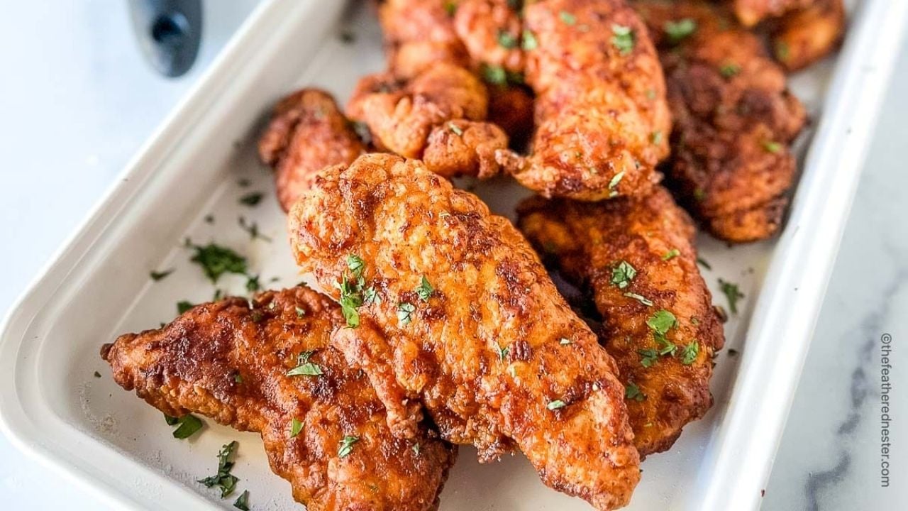 A white tray filled with crispy, golden brown fried chicken tenders, prepared Southern Supers style and garnished with chopped parsley—a true celebration of classic Southern food.