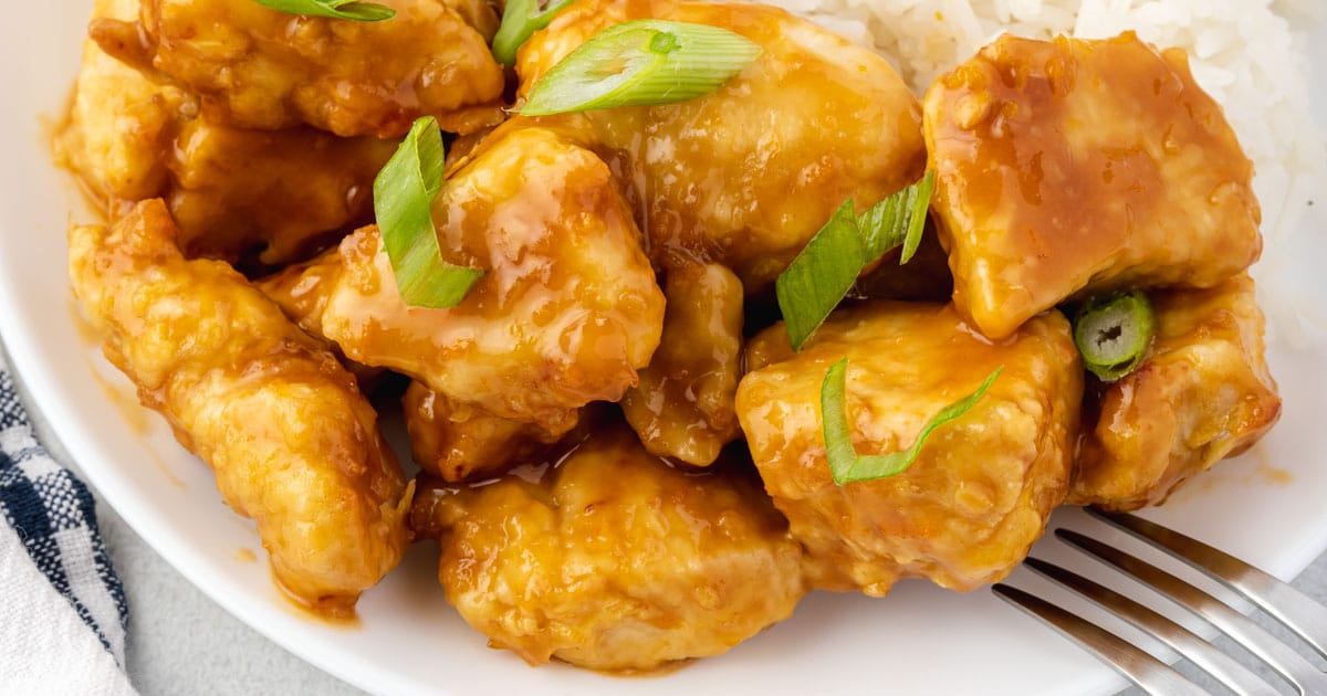Plate of orange chicken garnished with sliced green onions, served next to white rice, with a fork on the side—perfect for easy chicken dinners or quick weeknight dinners.