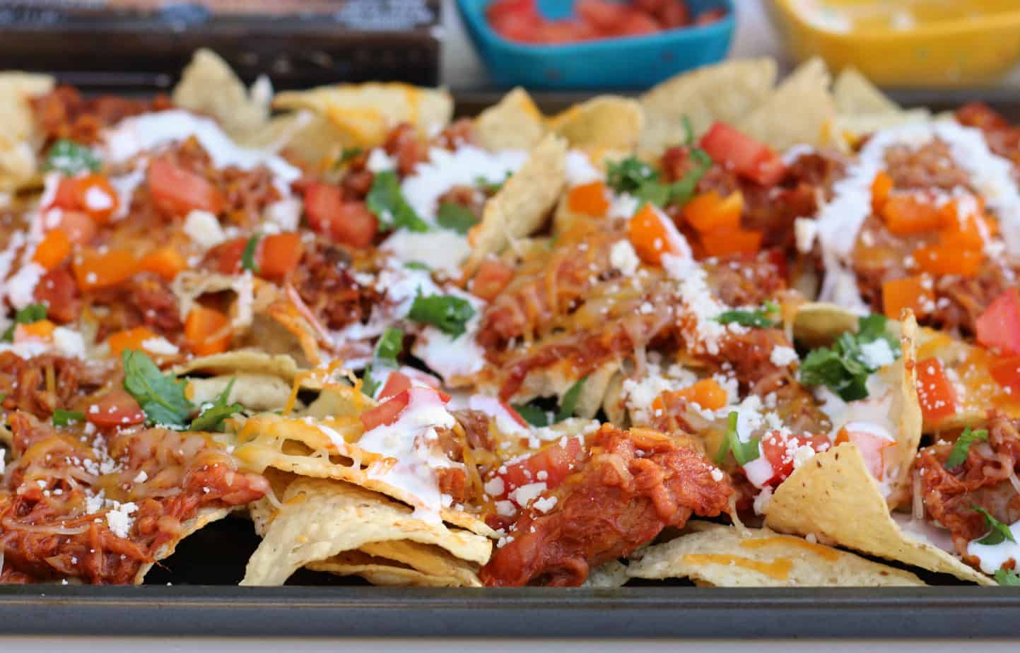 Tray of nachos topped with shredded chicken, melted cheese, chopped tomatoes, cilantro, and a drizzle of crema—perfect for easy dinners or as a crowd-pleasing sheet pan meal for busy weeknights.