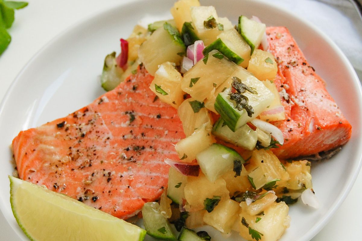 Grilled salmon fillet topped with pineapple cucumber salsa, served with a lime wedge on a white plate—perfect for those seeking popular recipes to add to their favorite saved recipes collection.