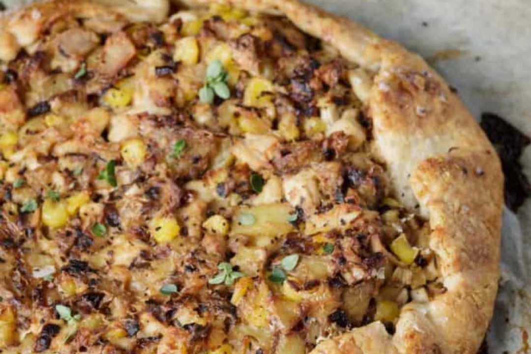 A rustic galette with a golden-brown crust filled with corn, onions, herbs, and shredded chicken, on parchment paper—a delicious twist for anyone seeking unique casserole recipes to try or save for later.