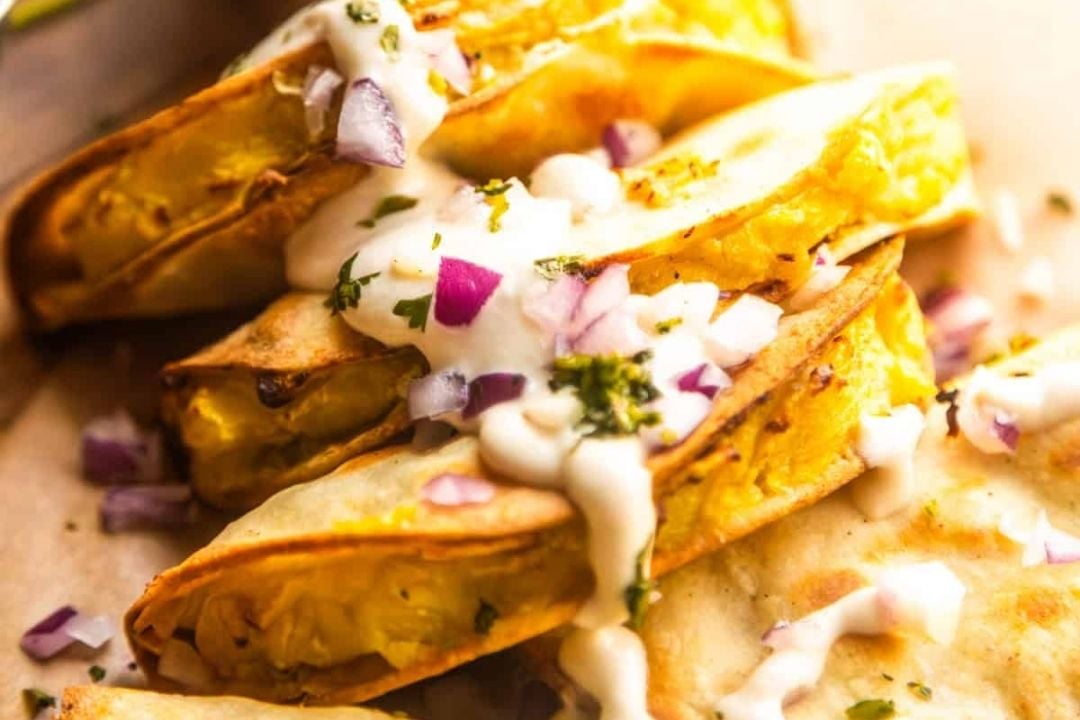 Three crispy tacos filled with shredded vegetables, topped with chopped red onions, fresh herbs, and drizzled with a creamy white sauce—one of the best potluck recipes to feed a crowd and keep your gatherings stress free.