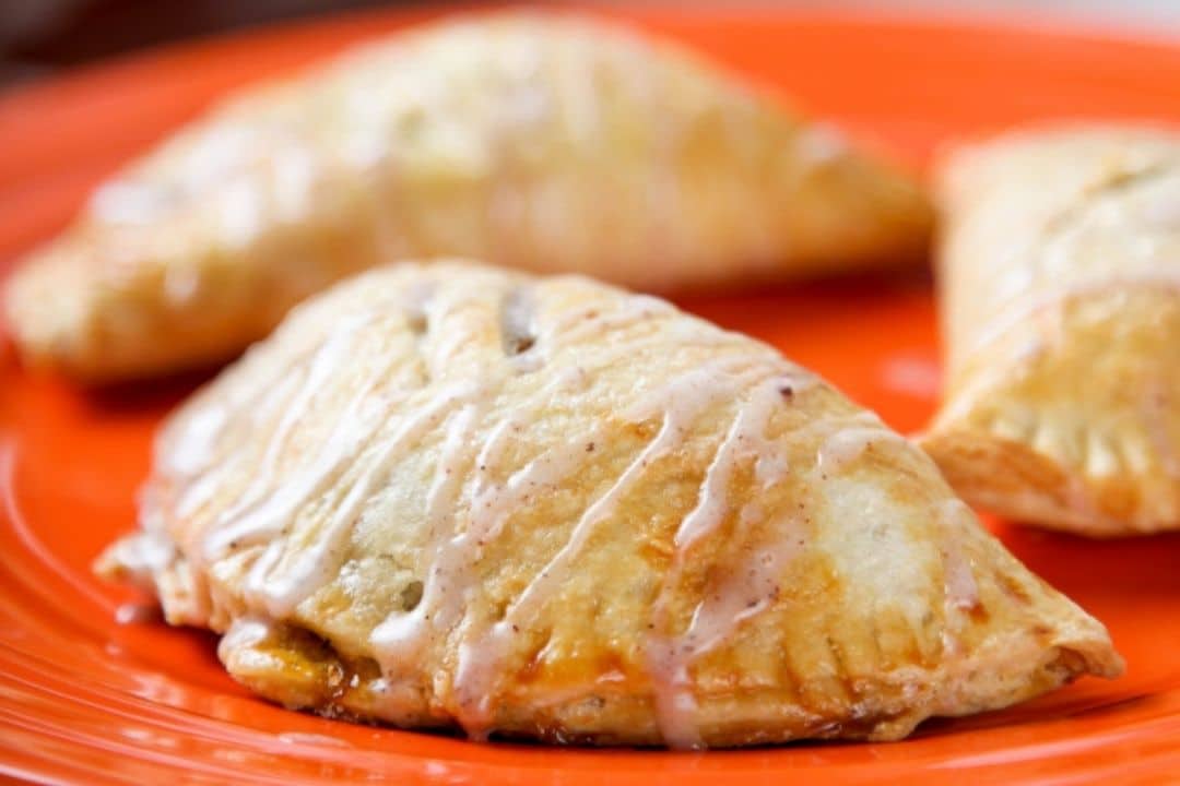 Three glazed, baked hand pies—perfect as easy desserts for kids—are displayed on an orange plate.