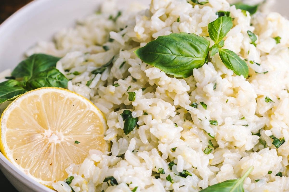 A bowl of cooked rice garnished with fresh basil leaves and a halved lemon, showcasing one of the most flavorful rice dishes perfect for those who love simple rice recipes.