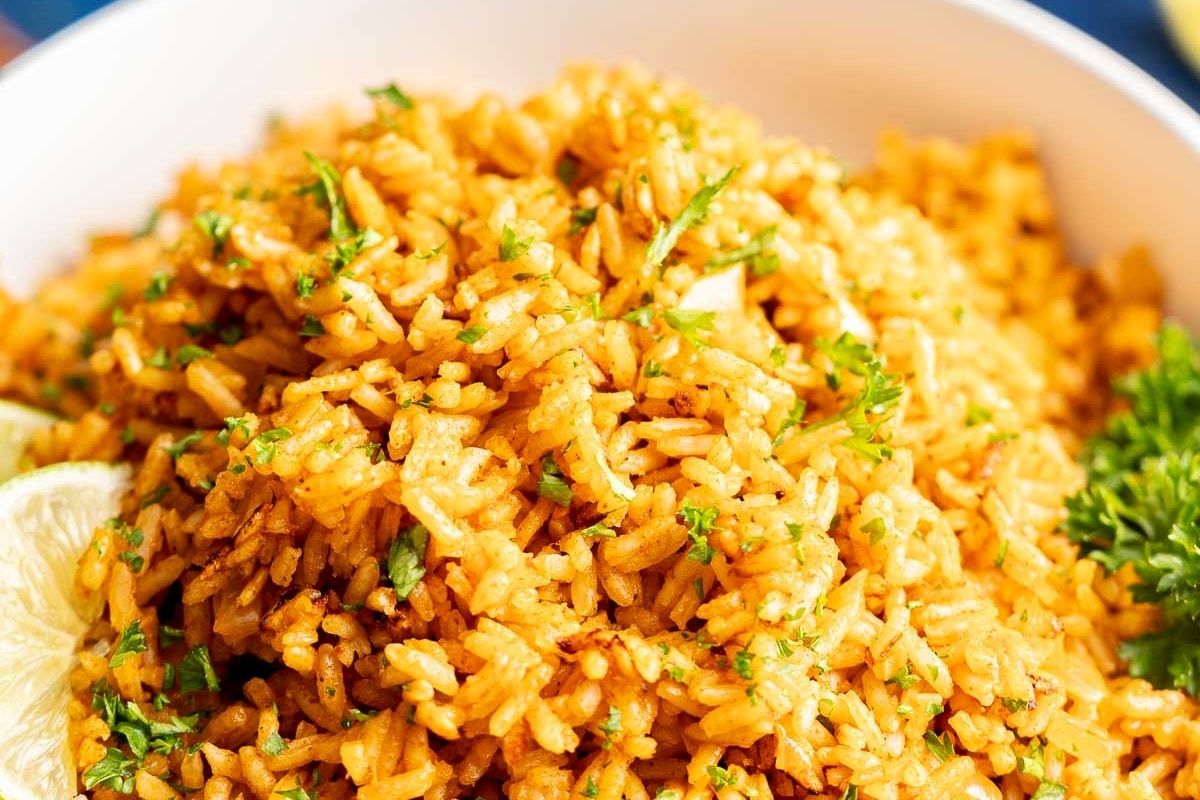 A close-up of flavorful rice, seasoned to perfection and garnished with chopped herbs, served in a white bowl with lemon wedges and a parsley sprig on the side.