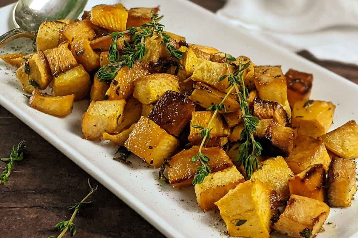 Roasted butternut squash cubes garnished with fresh thyme, served on a white rectangular plate—this flavor-packed recipe makes an irresistible addition to your collection of favorite side dishes.