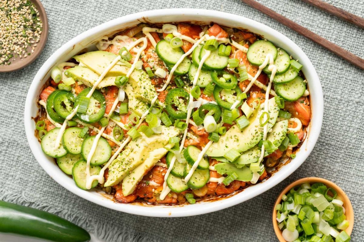 An oval dish filled with a baked casserole topped with sliced cucumber, avocado, jalapeños, green onions, mayonnaise drizzle, and seasoning—perfect for anyone looking for unique casserole recipes. Save for later if you’re searching for creative new casserole recipes to try!.