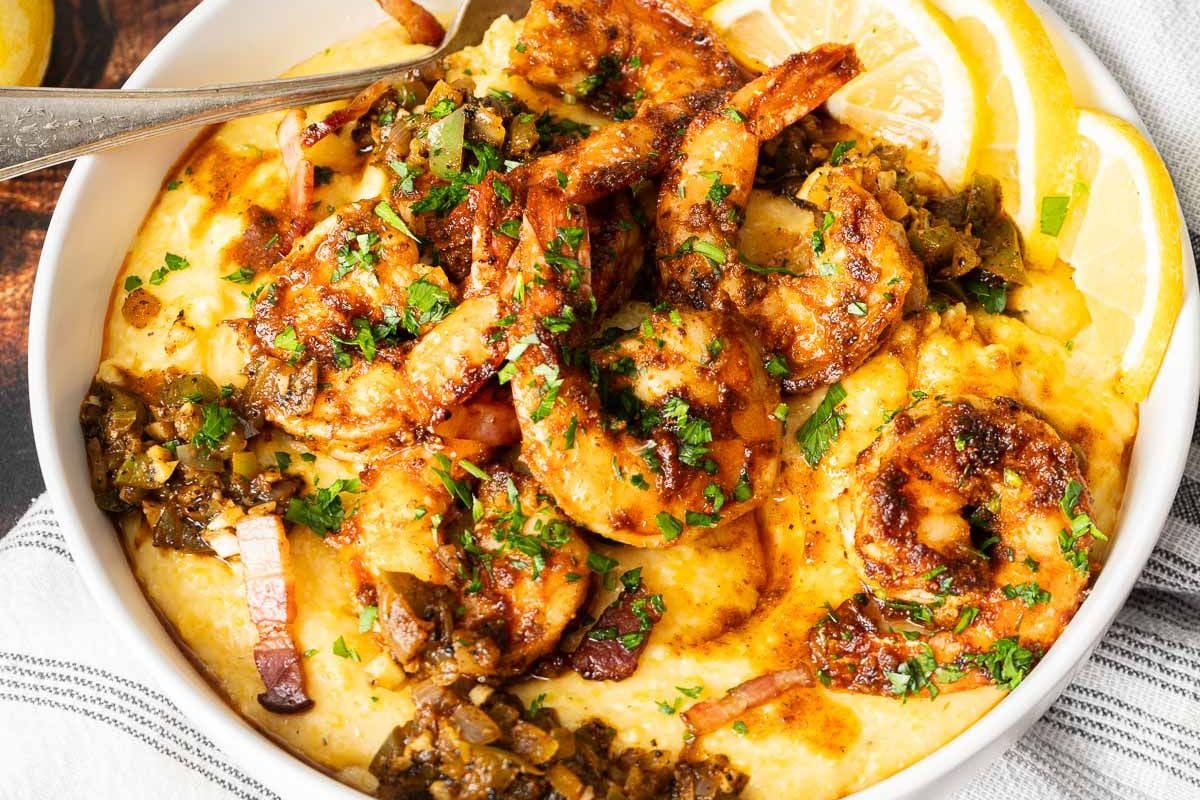 Bowl of shrimp and grits topped with sautéed vegetables, chopped herbs, and lemon slices on the side—a classic taste of Southern food that embodies the comforting flavors celebrated in Southern Supers.