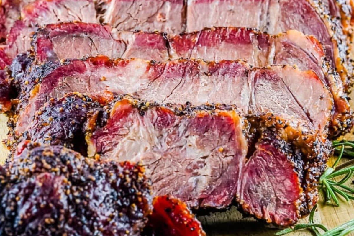 Sliced smoked beef brisket with a seasoned crust, arranged on a wooden surface with a sprig of rosemary nearby—a classic comfort food perfect for home cooking and cherished Sunday suppers.
