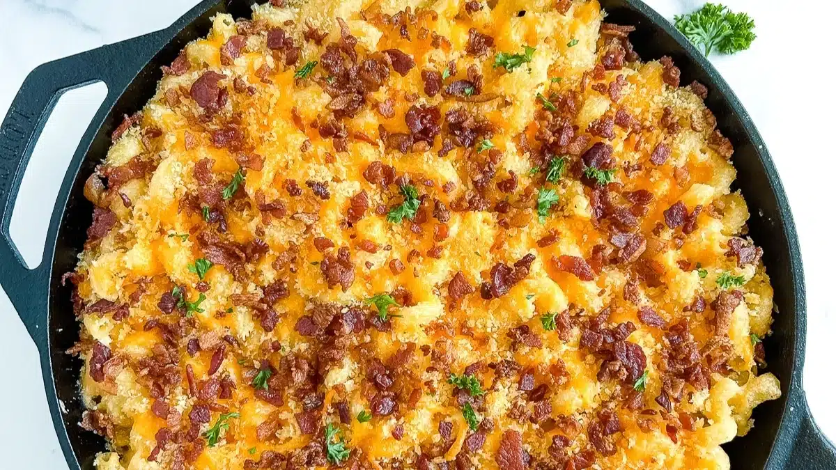 Baked macaroni and cheese topped with crispy bacon bits, melted cheddar cheese, and fresh parsley, served in a black cast iron skillet—this flavor-packed dish stands out among classic side dishes.