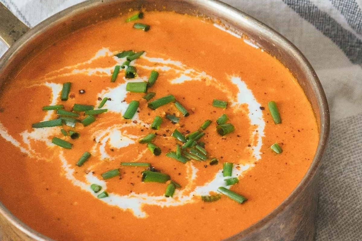 A bowl of creamy tomato soup garnished with a swirl of cream and chopped chives, placed on a cloth napkin—the perfect addition to your collection of cozy soup recipes for cool nights.