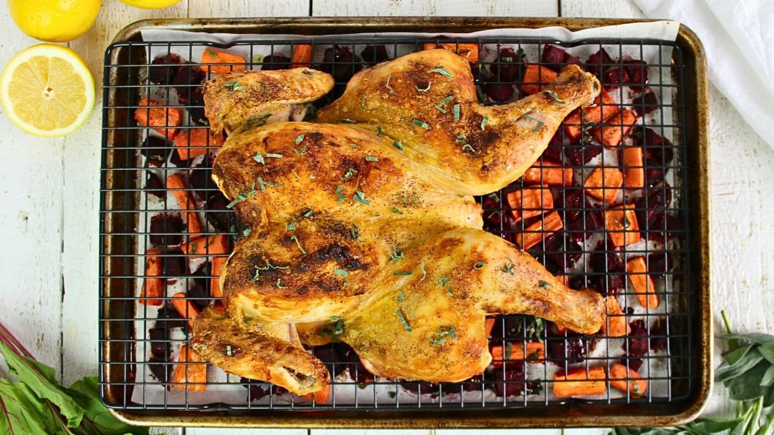 Roast spatchcock chicken on a wire rack over chopped carrots and beets on a baking sheet, with lemon halves on the side—one of the best easy chicken dinners perfect for new weeknight recipes.
