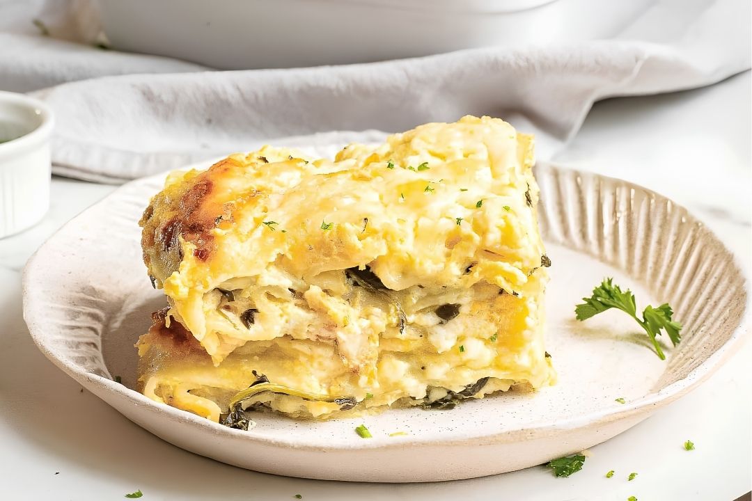 Two slices of creamy vegetable lasagna—perfect for cozy fall dinners—are served on a beige plate, garnished with chopped herbs and finished with a sprig of parsley on the side. This is one of those grandma-approved recipes that brings comfort to every bite.