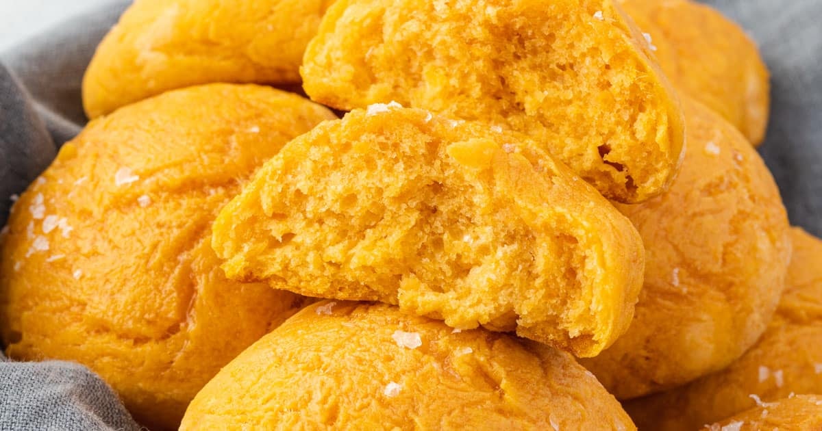 A close-up of several golden brown sweet potato biscuits, with one biscuit broken in half to show its soft, fluffy interior—perfect for serving as Thanksgiving side dishes.