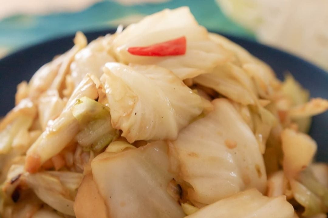 Stir-fried cabbage pieces with a slice of red chili on top, served on a dark plate—a simple yet flavorful addition to your favorite cabbage recipes.
