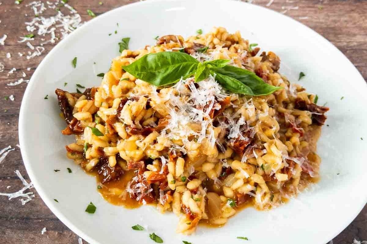 A plate of risotto garnished with grated cheese and fresh basil, served on a white dish with herbs sprinkled around—perfect for adding to your saved recipes or enjoying as one of your favorite dinner recipes.