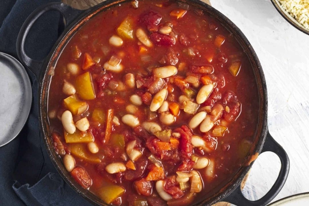 A pot filled with tomato-based vegetable and bean stew, containing white beans, diced tomatoes, carrots, and yellow bell peppers—perfect for those seeking comforting bean soups or exploring new bean soup recipes.